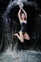 Girl dancer jumping and dancing in the white dust with flour on a black background. Studio shot of woman dancing with flour. photo