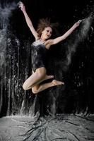 bailarina saltando y bailando en el polvo blanco con harina sobre un fondo negro. foto de estudio de mujer bailando con harina.