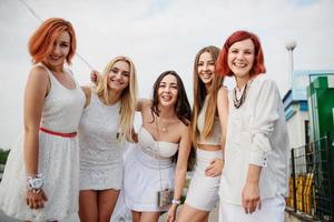 Five girls with balloons at hand weared on white dresses on hen party against pier on lake. photo