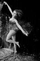 bailarina saltando y bailando en el polvo blanco con harina sobre un fondo negro. foto de estudio de mujer bailando con harina.