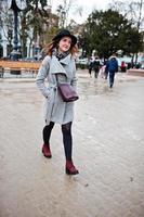 Young model tourist girl in a gray coat and black hat with leather handbag on shoulders posed at street of city. photo