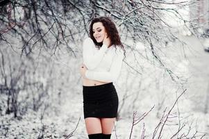 Curly brunette girl background falling snow, wear on black mini skirt and wool stockings. Model on winter. Fashion portrait at snowy weather. Instagram toned photo. photo