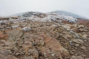 Frozen rocky stones at snow mountains with frost grass and fog on top photo