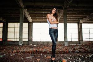 Portrait of young cute brunette girl wearing on black leather pants and white blouse posed on abandoned place. photo