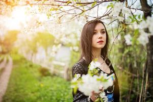 Cierra el retrato de una joven morena con flor de cerezo en el jardín de primavera. foto