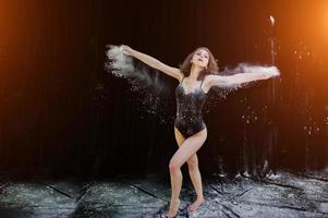 Girl dancer jumping and dancing in the white dust with flour on a black background. Studio shot of woman dancing with flour. photo