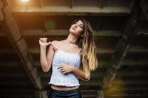 retrato de una joven morena linda con pantalones de cuero negro y blusa blanca posada en un lugar abandonado. foto