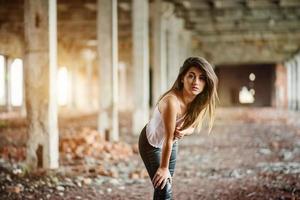 retrato de una joven morena linda con pantalones de cuero negro y blusa blanca posada en un lugar abandonado. foto