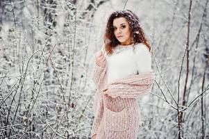 Curly brunette girl background falling snow, wear on warm knitted sweater, black mini skirt and wool stockings. Model on winter. Fashion portrait at snowy weather. Instagram toned photo. photo