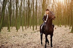 Young stylish blonde girl riding on horses at autumn forest. photo