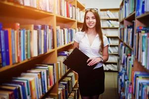 Brunette girl at library with folder of documents, wear on white blouse and black mini skirt. Sexy business woman or teacher concept. Smile on braces.