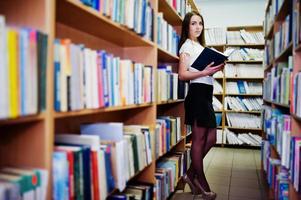 Brunette girl at library with folder of documents, wear on white blouse and black mini skirt. Sexy business woman or teacher concept. photo