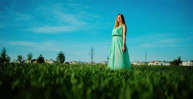 mujer con un hermoso vestido largo turquesa posando en un prado sobre hierba. foto