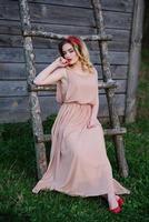 yong elegancia chica rubia en vestido de rosa en la escalera de madera de fondo de jardín. foto