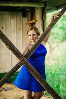 joven con sobrepeso en vestido azul plantea jardín de primavera de fondo en cabaña de madera.