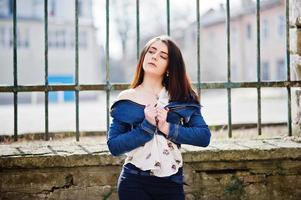 Young stylish brunette girl on shirt, pants, jeans jacket  posed background iron fence. Street fashion model concept. photo