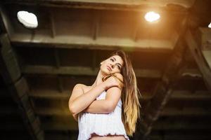 retrato de una joven morena linda con pantalones de cuero negro y blusa blanca posada en un lugar abandonado. foto