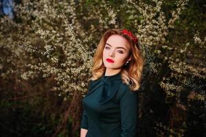 Close up portrait of yong elegance blonde girl at green dress on the garden in spring on blossom trees. photo