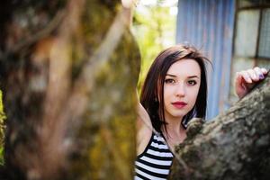 Brunette model girl at dress with stripes posed near tree. photo