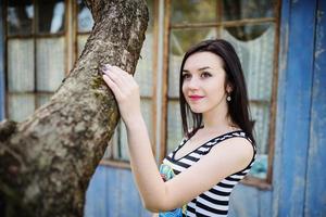 Brunette model girl at dress with stripes posed near tree. photo