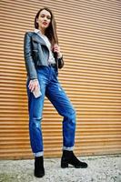 Portrait of stylish young girl wear on leather jacket and ripped jeans with mobile phone at hand background shutter texture. Street fashion model style.