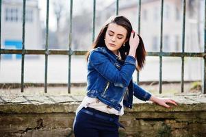 joven morena con estilo en camisa, pantalones, chaqueta de jeans posada cerca de hierro de fondo. concepto de modelo de moda callejera. foto