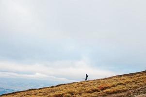 Man with a back pack walking down the mountain with stick at hand. photo