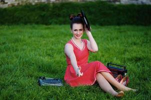 Portrait of young pinup girl wearing at retro vintage old-fashioned dress in peas sitting on grass wit retro radio and vinyl audio record in hands. photo