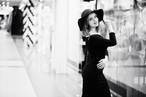 ropa de niña pelirroja de moda con vestido negro y sombrero rojo posado en el centro comercial comercial. foto en blanco y negro.