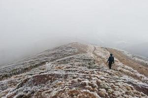 Tourist photographer with tripod on hand walking on frozen hill with fog. photo