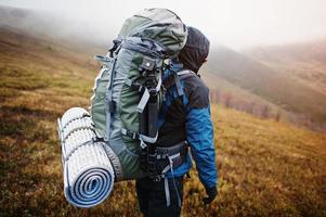 vista de cerca de las esteras y el trípode de la mochila turística trasera, vistiendo una chaqueta de turismo azul con capucha y de pie en la montaña foto