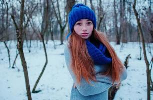 retrato de una joven pelirroja con pecas con sombrero de lana de punto azul y bufanda en el día de invierno. foto