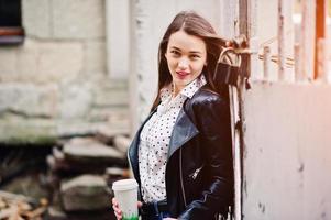 retrato de una joven elegante vestida con una chaqueta de cuero y jeans rotos con una taza de café. estilo de modelo de moda callejera. foto