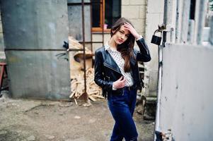 retrato de una joven elegante vestida con una chaqueta de cuero y jeans rotos en las calles de la ciudad. estilo de modelo de moda callejera. foto