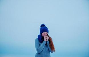 Portrait of young red hair girl with freckles wearing at blue knitted wool hat and scarf in winter day background ice. photo