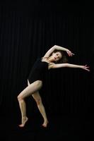 Girl dancer jumping and dancing on a black background. Studio shot of woman dancing. photo