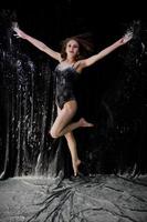 Girl dancer jumping and dancing in the white dust with flour on a black background. Studio shot of woman dancing with flour. photo