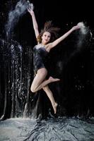 bailarina saltando y bailando en el polvo blanco con harina sobre un fondo negro. foto de estudio de mujer bailando con harina.