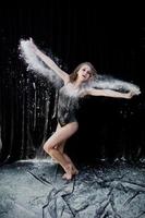 Girl dancer jumping and dancing in the white dust with flour on a black background. Studio shot of woman dancing with flour. photo