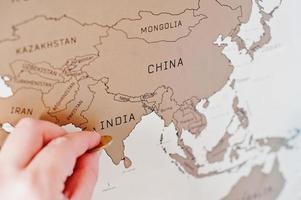 Rascar el mapa de viaje del mundo. mano de hombre borrar india con moneda. foto