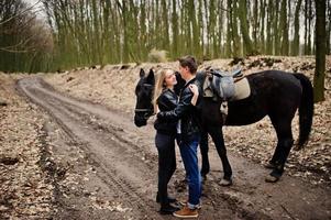 joven pareja elegante enamorada cerca de caballo en el bosque de otoño. foto