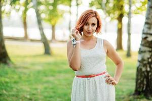 Portrait of red haired girl wearing on white dress against park at hen party. photo