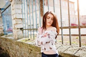 Young stylish brunette girl on shirt with cats and blue pants posed background iron fence. Street fashion model concept. photo
