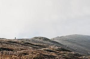 hombre en la cima de la colina helada, caminando hacia arriba. increíble paisaje de la gente y la montaña. foto