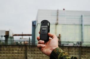 dosímetro a mano y planta de energía nuclear en el fondo foto