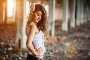 Portrait of young cute brunette girl wearing on black leather pants and white blouse posed on abandoned place. photo