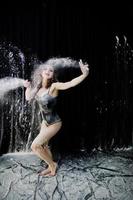 Girl dancer jumping and dancing in the white dust with flour on a black background. Studio shot of woman dancing with flour. photo