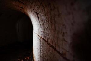 túnel de arco de ladrillo aterrador en la oscuridad y algo de luz. foto