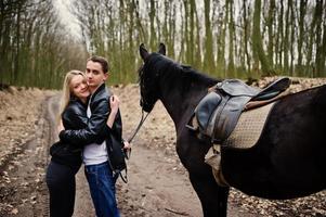 joven pareja elegante enamorada cerca de caballo en el bosque de otoño. foto
