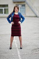 Young chubby teenage girl wear on red dress and jeans jacket posed against school backyard. photo